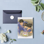 Load image into Gallery viewer, Arab family illustrated birthday card showing a father and two children leaning over a white cake with whipped cream and red cherries. Father wears blue knock-off Nike sweats, and the boy wears a CEIKO digital watch. Handwritten labels highlight details like ‘Dad’s knock off Nike Sweats,’ ‘Cherries that no one eats,’ and ‘Gateaux Nabil Fancy Cake.’ Card sits on a brown envelope with wax seal and dried flowers. Arab family gift, birthday card, nostalgic design.

